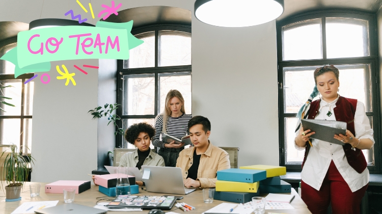 Tim zaposlenih sedi oko stola u modernoj kancelariji dok rade na laptopovima i dokumentima, sa grafičkim natpisom “Go Team” u gornjem levom uglu.